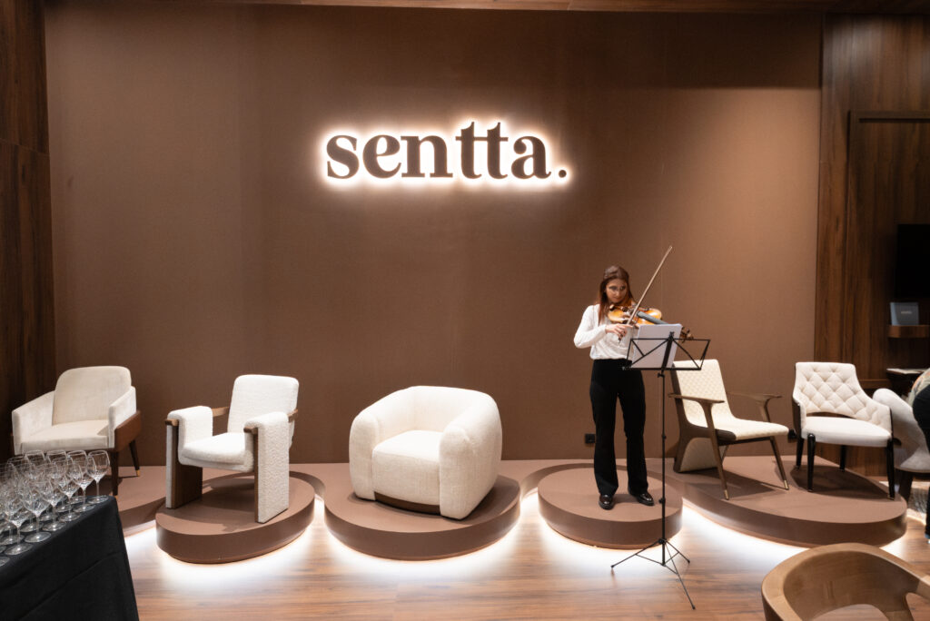 The cénic atmosphere of the Sentta stand at Salone del Mobile 2026, featuring the new Vellure, Floow, Avoria, and Kado armchairs during the exclusive April 23 event.